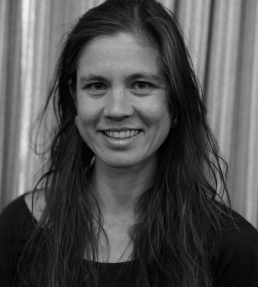 Black and White portrait of Georgiana de Rham. She has brown hair, earrings, and a dark colored tee shirt.