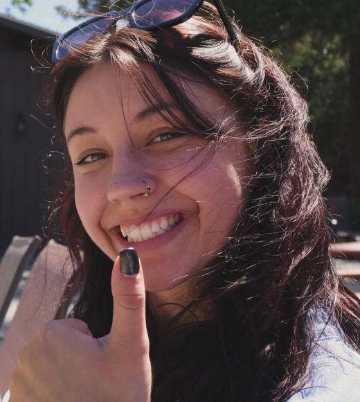 A close up picture of Ellie smiling and holding a "thumbs up"