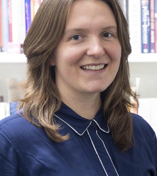 Image of woman with brown hair and a blue shirt with books in the background