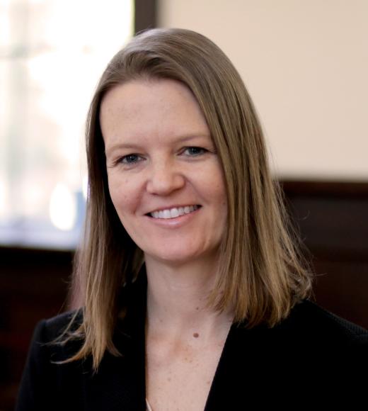 Smiling woman with shoulder-length brown hair wearing black blazer in office