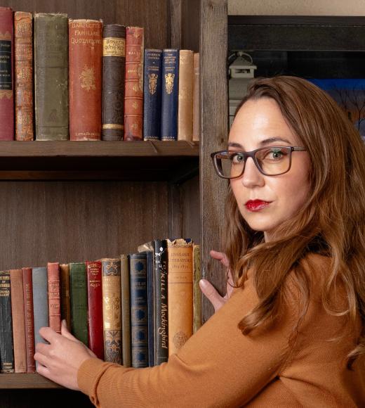Heather stands at her bookshelf grabbing a copy of John Leyden's Scenes of Infancy