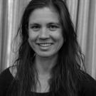 Black and White portrait of Georgiana de Rham. She has brown hair, earrings, and a dark colored tee shirt.