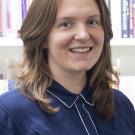 Image of woman with brown hair and a blue shirt with books in the background