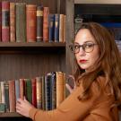 Heather stands at her bookshelf grabbing a copy of John Leyden's Scenes of Infancy